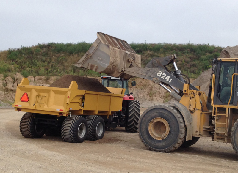 The 20 ton off-road dumper trailer hooked up to a tractor while getting dirt dumped into it